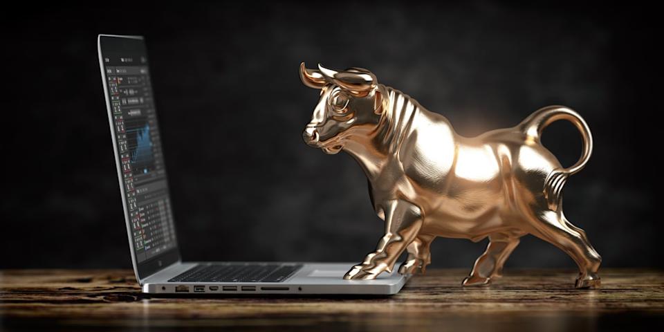 A golden bull looking at stock charts on a laptop.