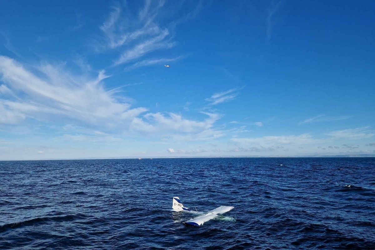 An aircraft, potentially a drone, is partially submerged in a body of water, possibly the ocean, with the wings above the water surface.