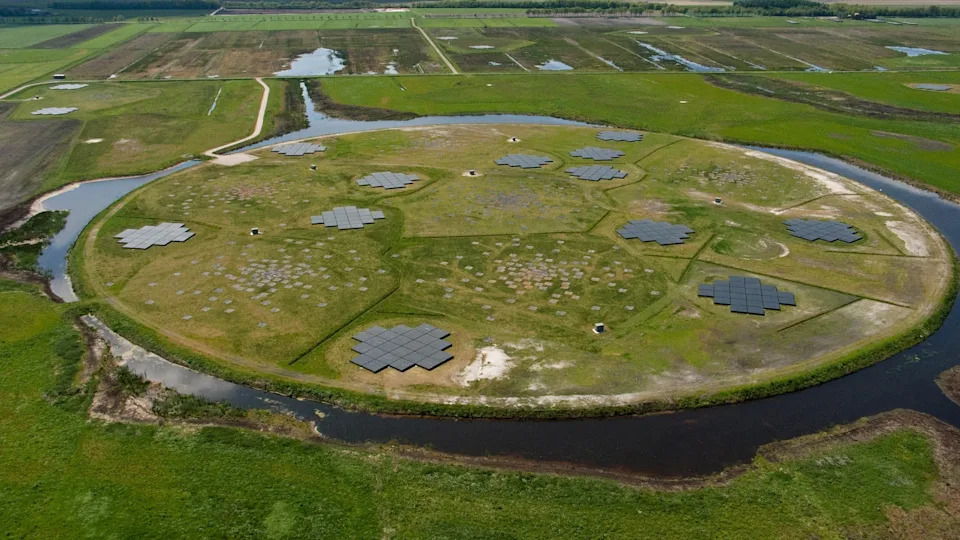 an aerial view of a round plot of land circled by a canal. on the round plot of land are arrays of square-shaped pieces of glass