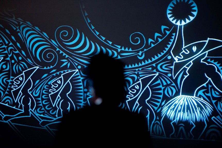 A silhouette of a person looking at patterned blue illuminated art installation.