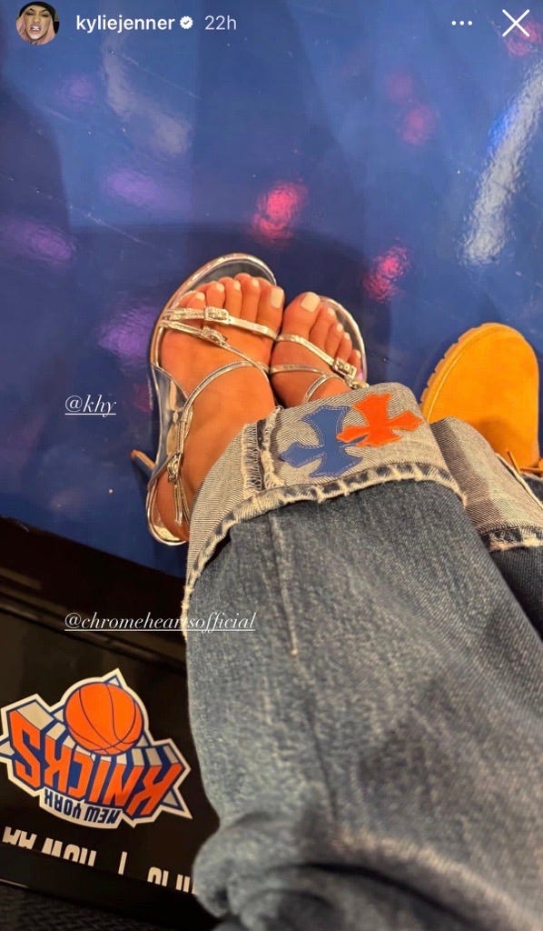 Feet in silver sandals next to Knicks logo on floor. Feet in silver sandals next to Knicks logo on floor.