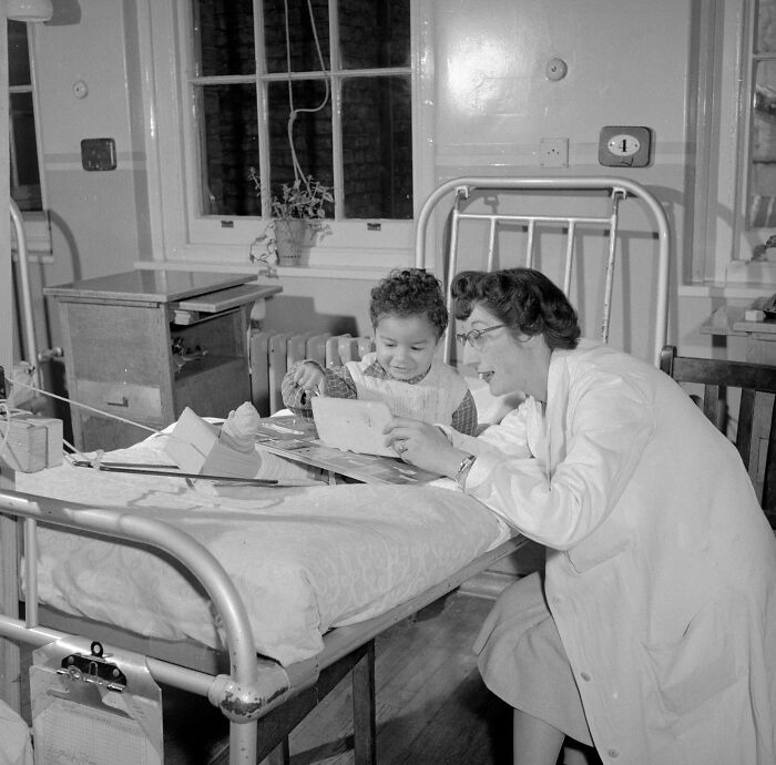 A nurse helping a child patient read in a hospital bed, one of the things nurses encounter with their patients.