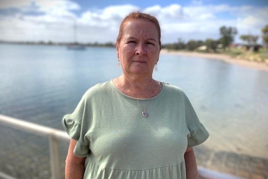 Image of Monica wearing a t shirt and her hair tied back. She stands in front of the ocean and looks concerned at camera.