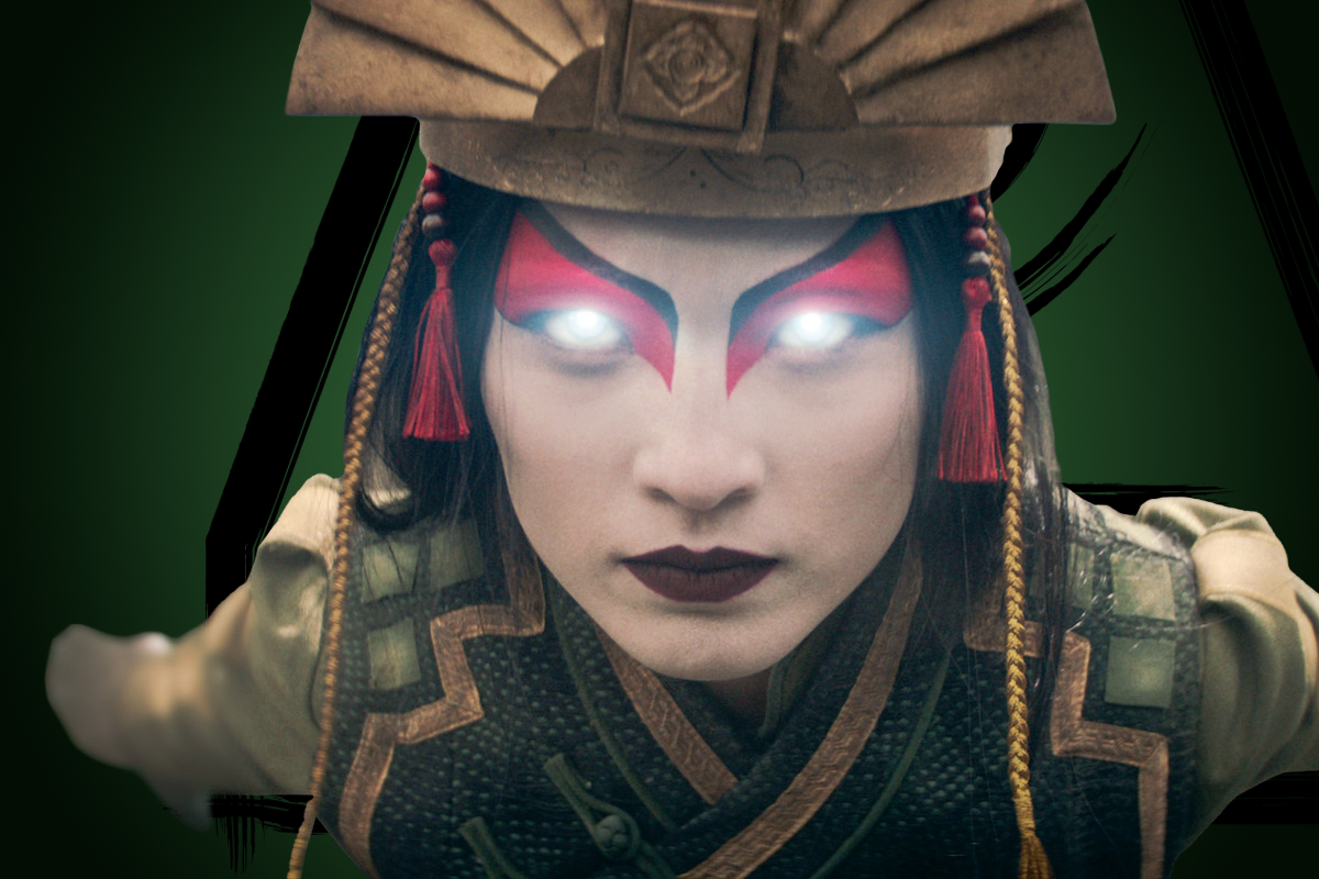 Yvonne Chapman as Avatar Kyoshi in ornate, fantasy armor with glowing white eyes, dramatic red and black makeup, and a large headdress, set against a dark green background, suggesting a mystical or supernatural setting.