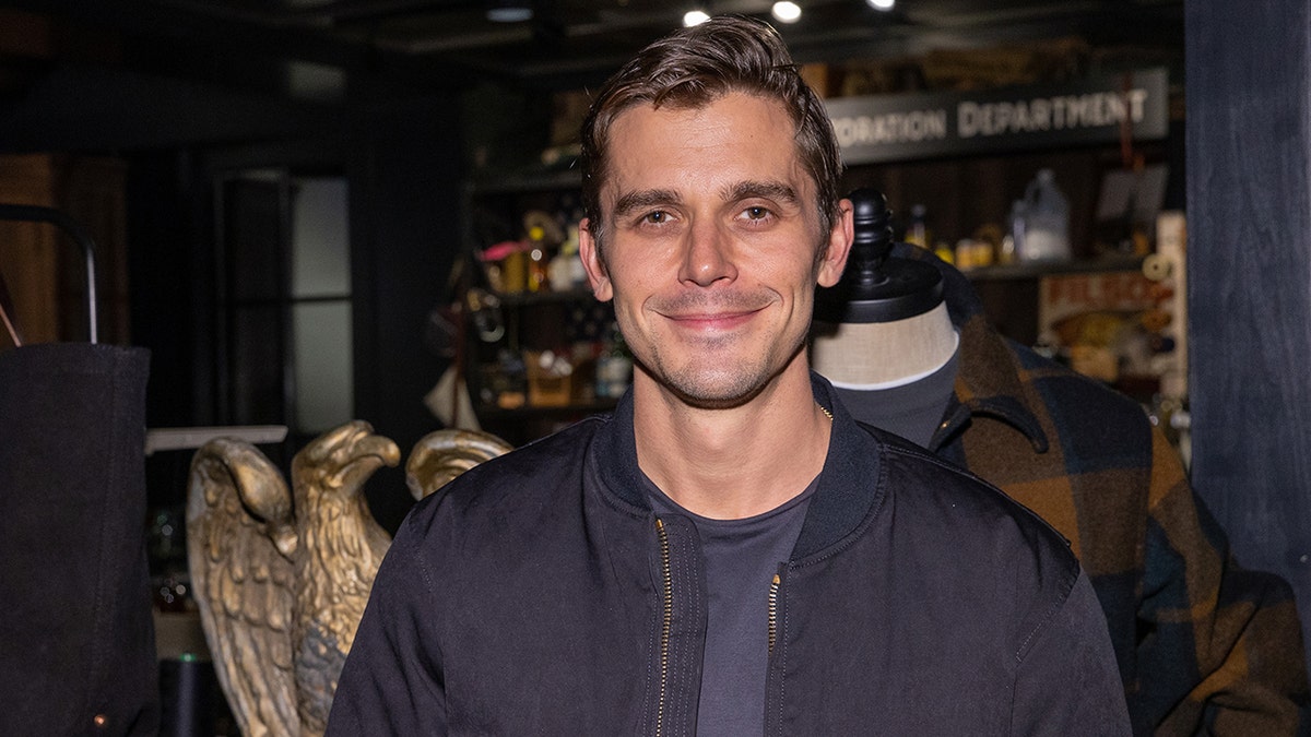 Antoni Porowski smiling softly wearing a navy jacket and shirt in Seattle.