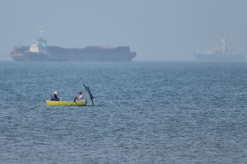 Two men sit in a small boat as cargo ships are anchored in the background in the Strait of Hormuz. Photograph: Amirhosein Khorgooi/AP