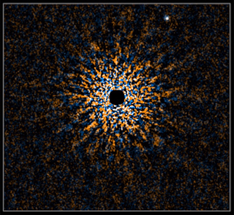 Small black circle surrounded by bright, multi-colored and pixelated rays stretching outward from it. A smaller whitish dot is in the upper right.