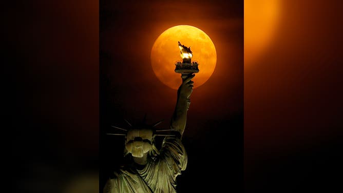 The Buck Moon rises through a haze behind the Statue of Liberty in New York City on July 2, 2023, as seen from Jersey City, New Jersey.