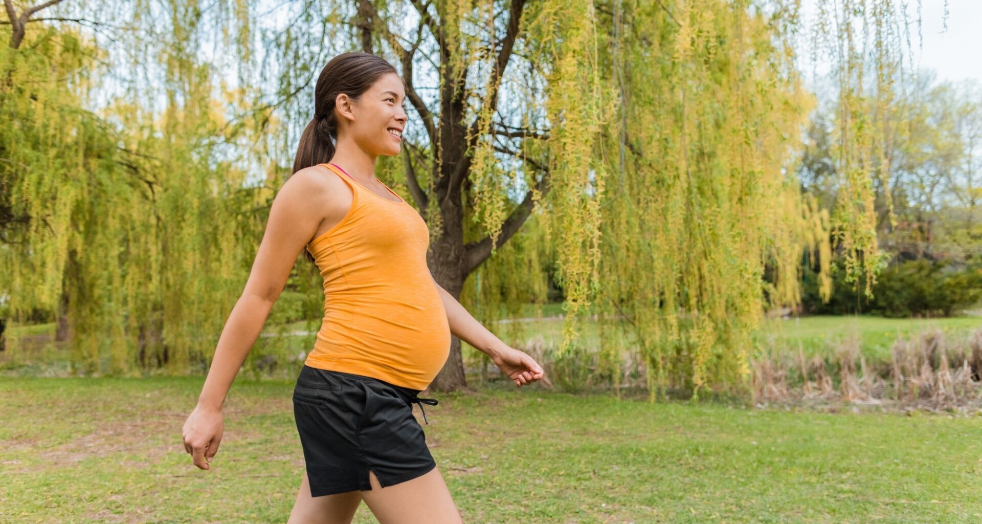 Pregnant woman walking outside in city park during summer for healthy active body workout