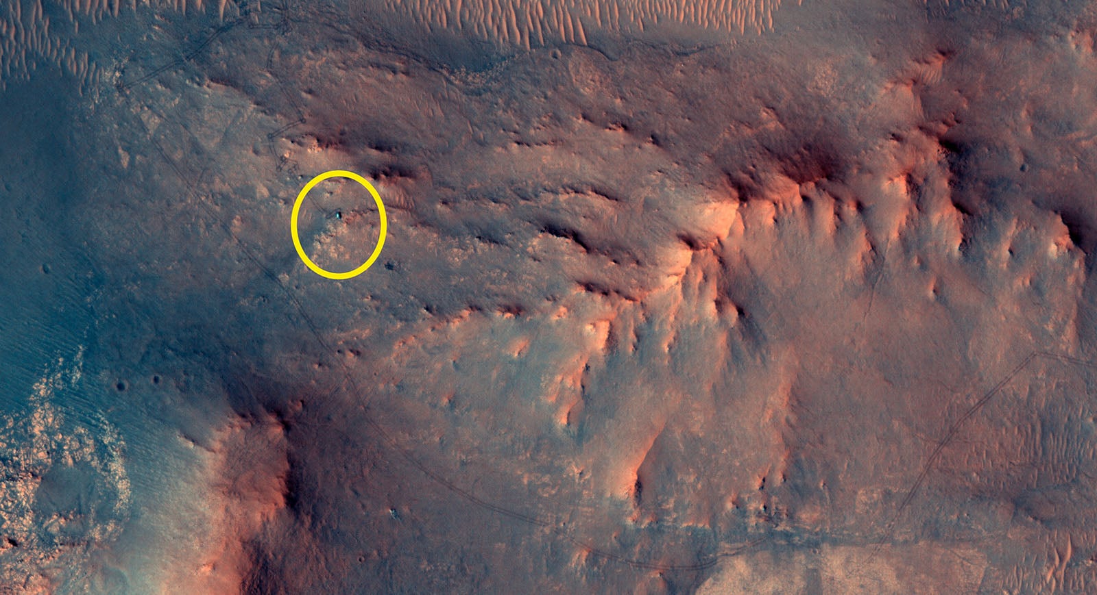 A rocky, reddish Martian landscape with ridges and shadows. A yellow circle highlights a specific area near the center left of the image, drawing attention to a feature on the Martian surface.