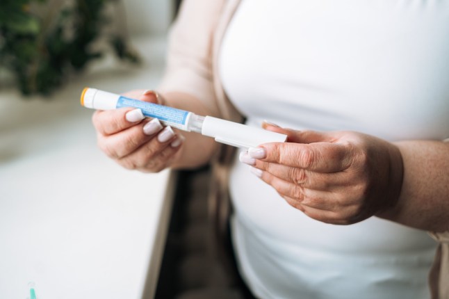 Plus-size woman gripping a prescription weight loss pen injector near a residential window. Concept of GLP-1 therapy, self-administered injection, home-based obesity management, and healthy lifestyle change