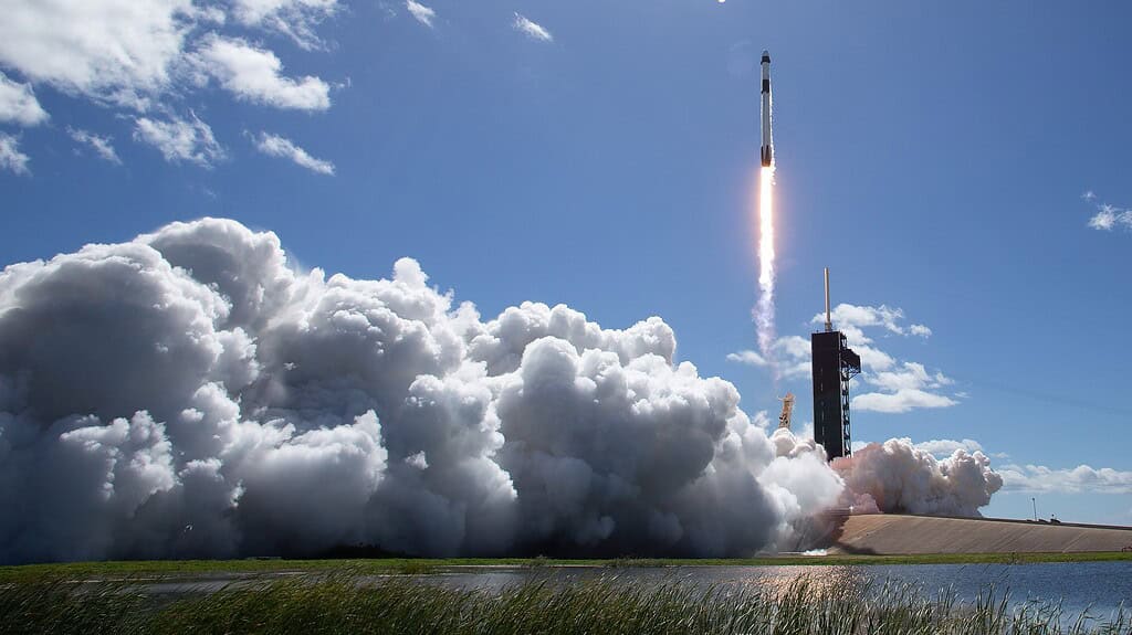 Rocket launch with smoke and flames, bright sky, and clouds in the background.