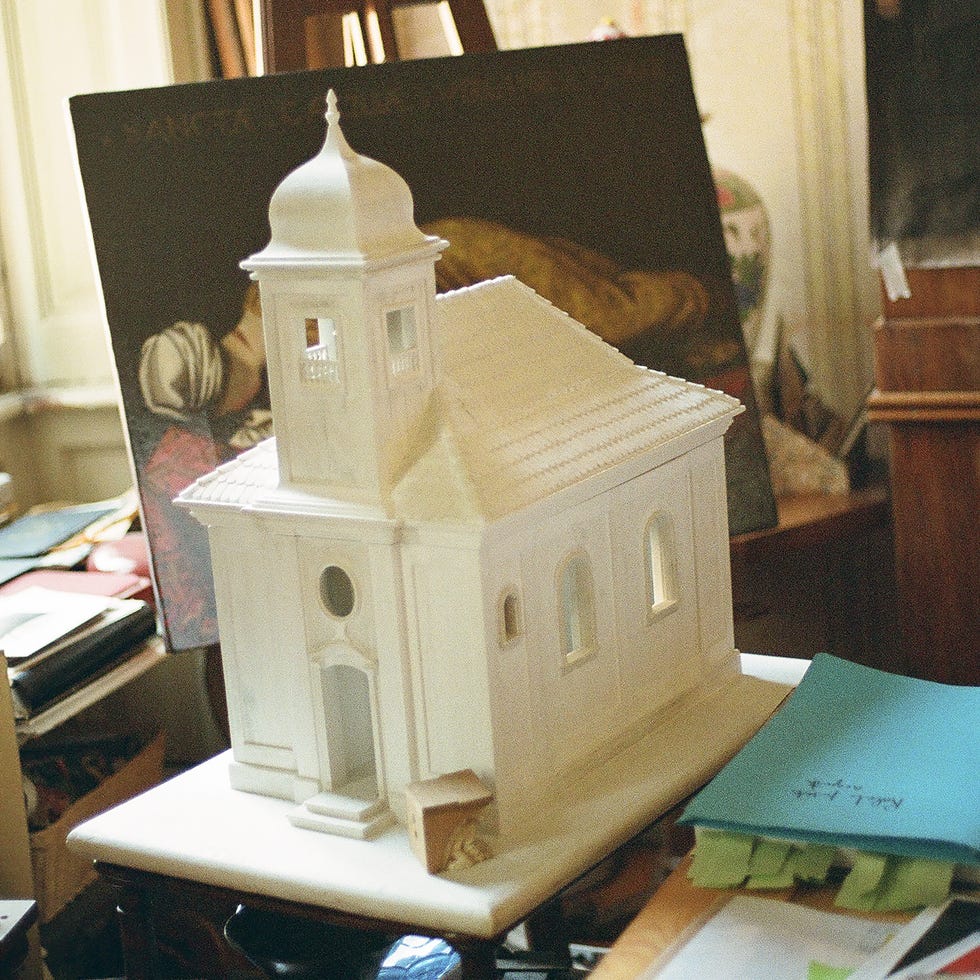 Miniature model of a white church on a wooden table with books and papers nearby.