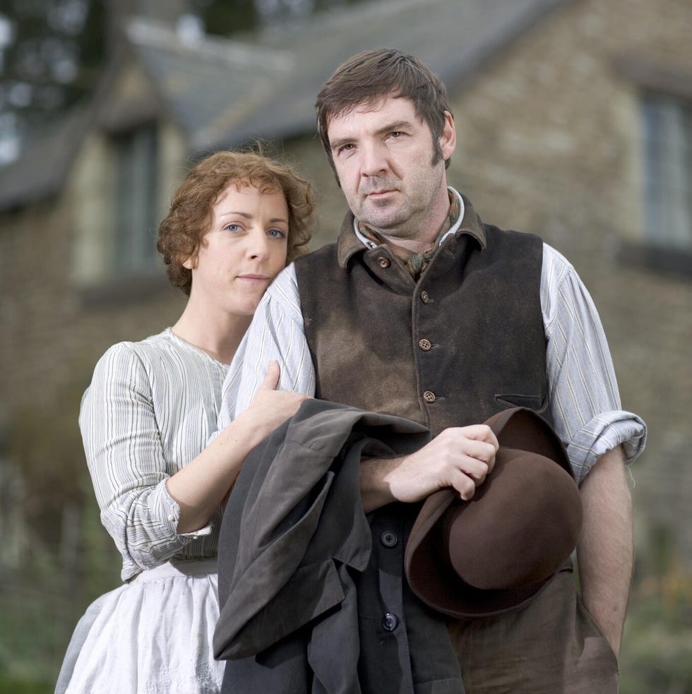 two individuals standing close together outdoors with a house in the background