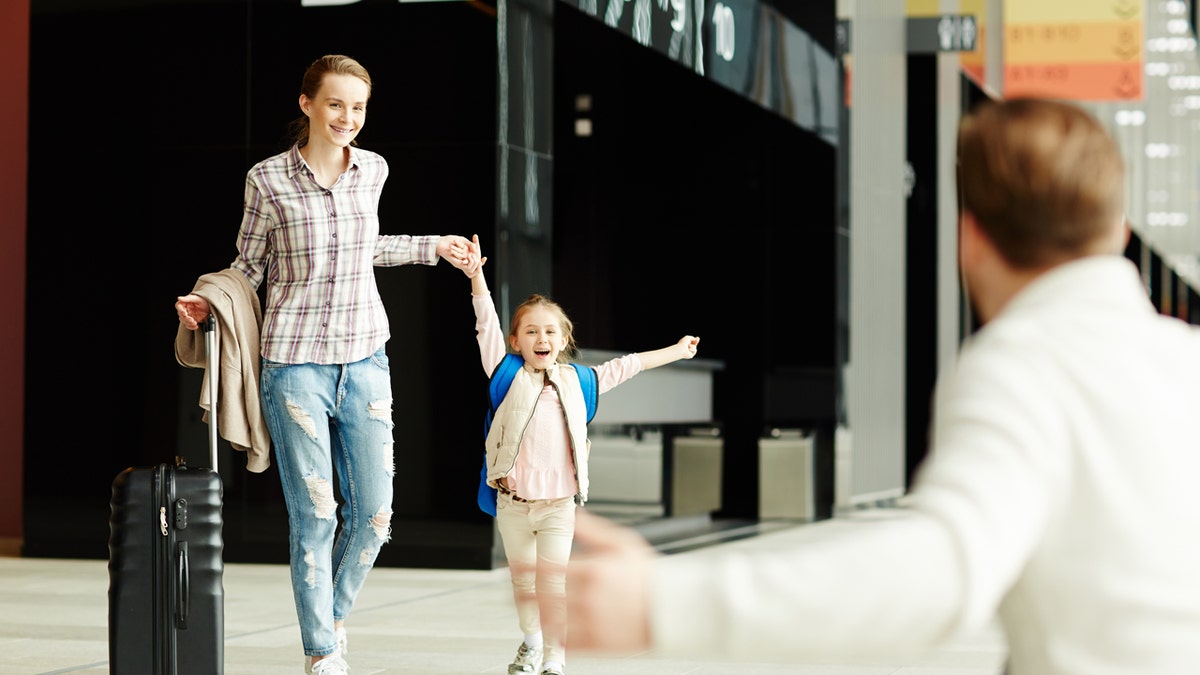 Dad putting his arm out to hug daughter and wife at airport