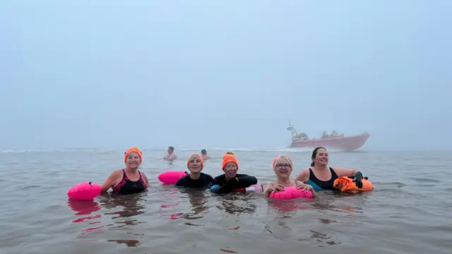 A group of women in the foggy sea. An RNLI lifeboat is behind them.