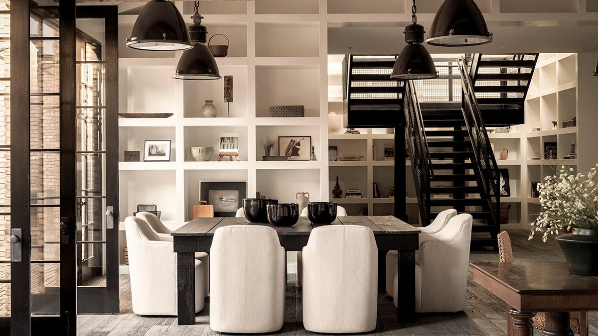 A black dining room table with a unique staircase behind it