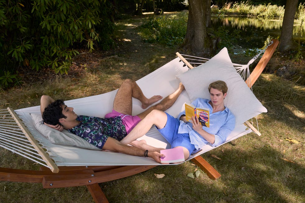 Two people relaxing on a hammock; one reading a book, the other dozing off.