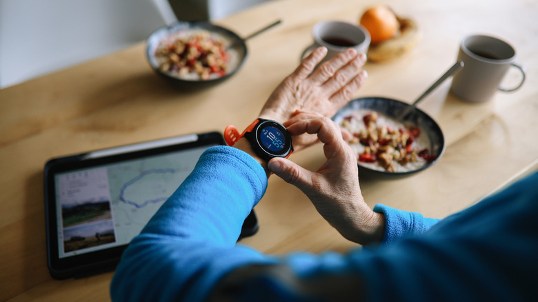 An older person adjusts their smartwatch while eating breakfast.
