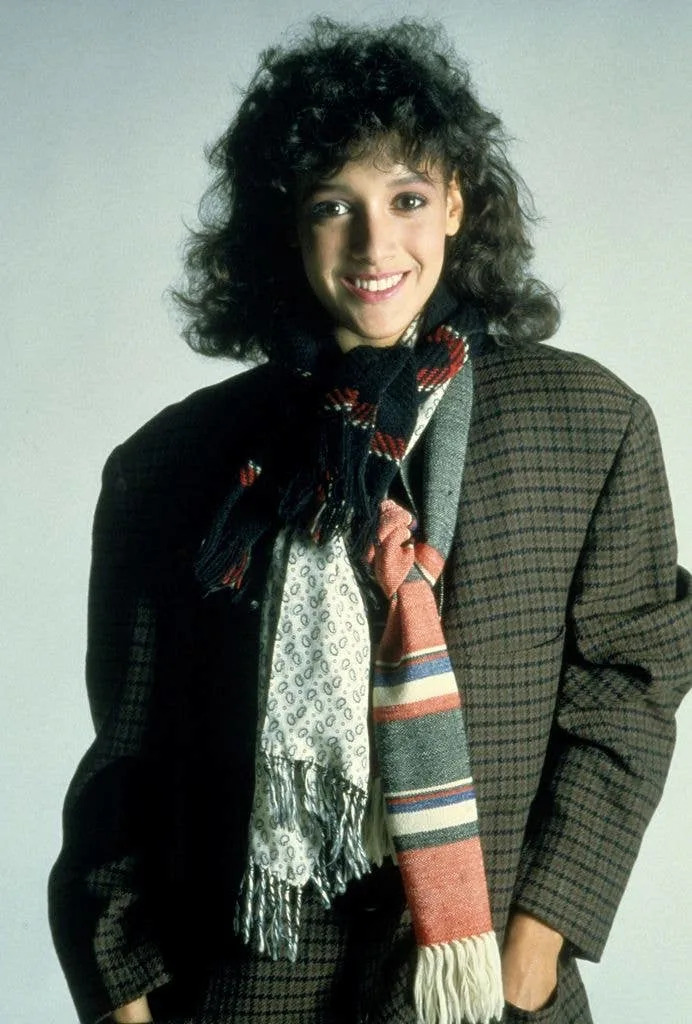 Jennifer Beals in a patterned and striped scarf and oversized green check jacket in 1983.