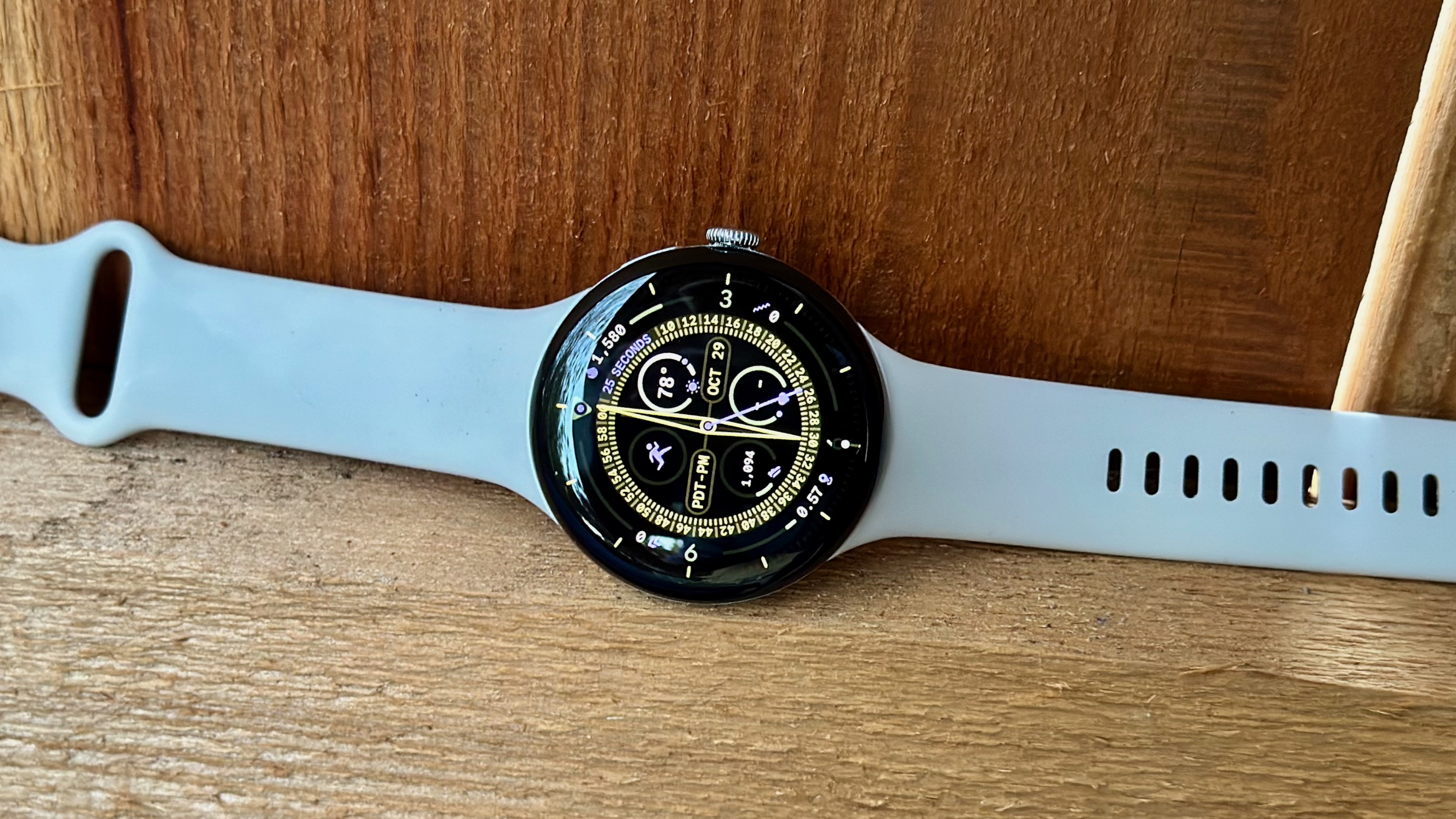A photo of the Google Pixel Watch 4 sitting on a brown fence board, showing the Expedition watch face
