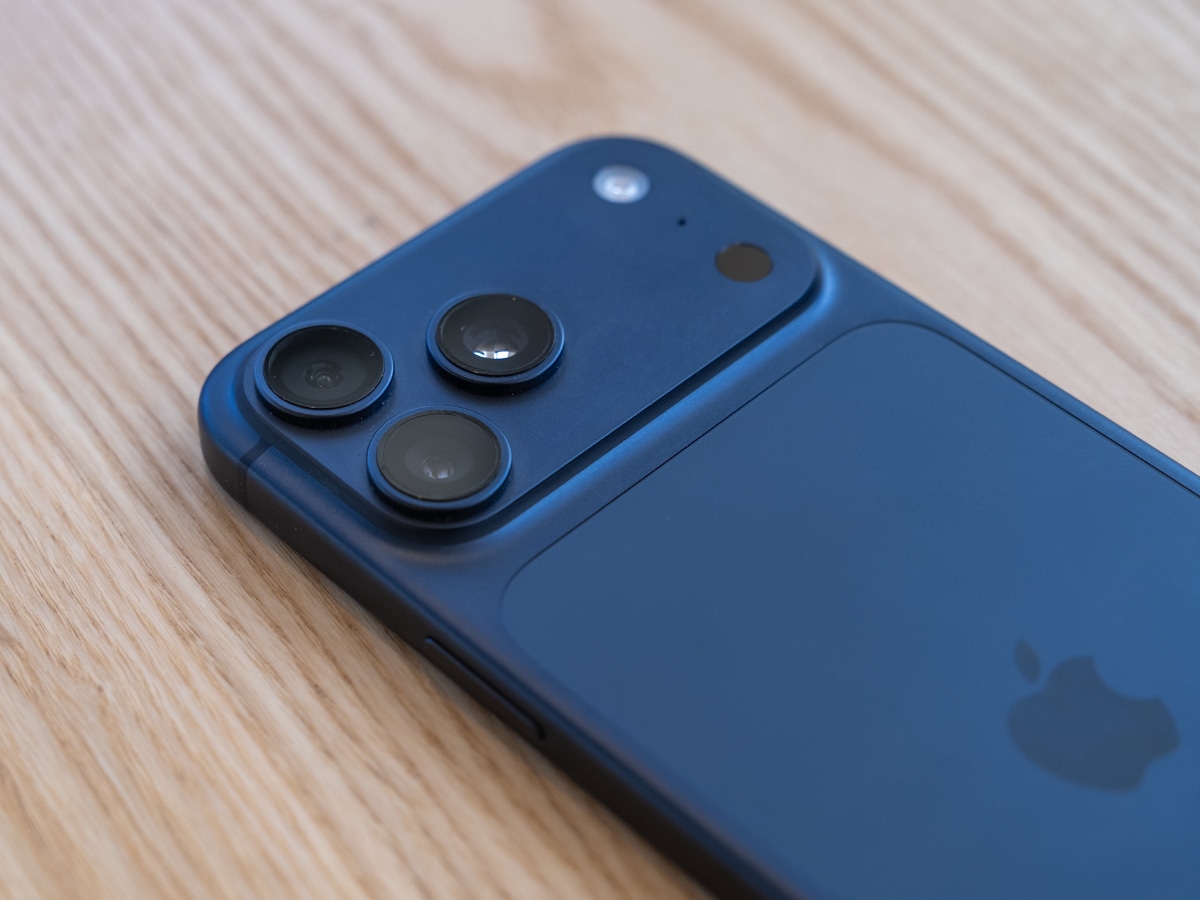 iPhone 17 Pro Max in deep blue showing rear camera lenses on a wooden surface.