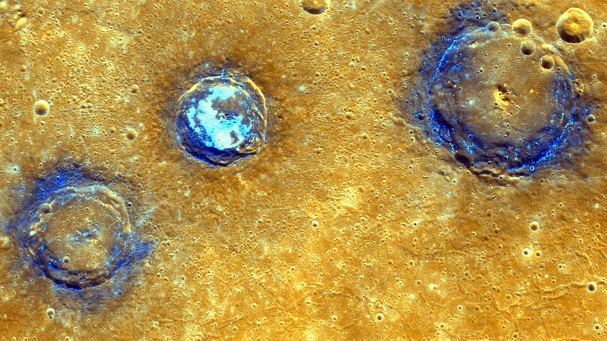 An image of the surface of Mercury shows a yellow surface and three craters ringed with dark blue. The middle crater has light blue spots in the center, and the other two are dotted with light blue around the edges.