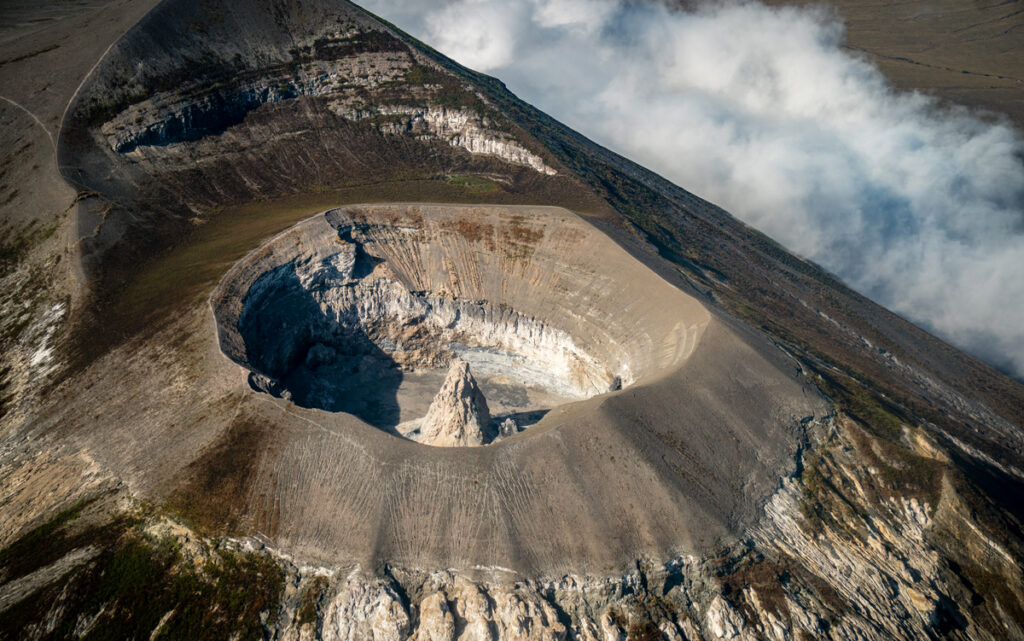 Aerial view of a volcano, a large crater with a sharp peak at its center