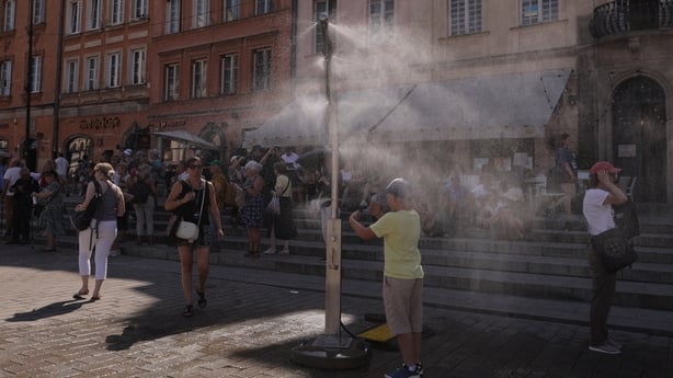 People cool off under a sprinkler during a heatwave at the Old Town in Warsaw