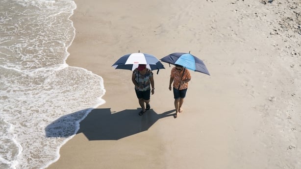 People walk with umbrellas on the beach during a heatwave in Carolina Beach, North Carolina, on July 3, 2026. Blistering temperatures and humidity has gripped swaths of the United States this week, with more to come for the densely populated East Coast as the nation co-hosts the World Cup and prepar