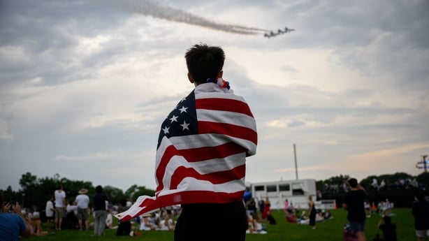 An attendee wrapped in a US flag watches a flyover near the Washington Monument.