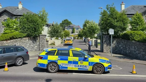 A garda car is seen blocking the entrance to a road with uniformed gardai in the background