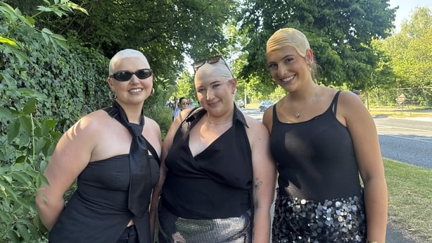 Three young women wearing bald caps, sparkly skirts and black tops