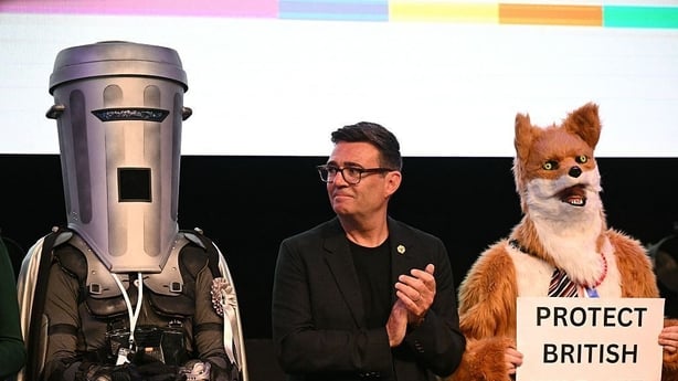 A man dressed as a bin stands next to another man who applauds him