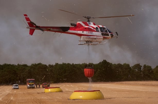 Firefighting helicopters with a suspended water bucket collect water from a temporary reservoir