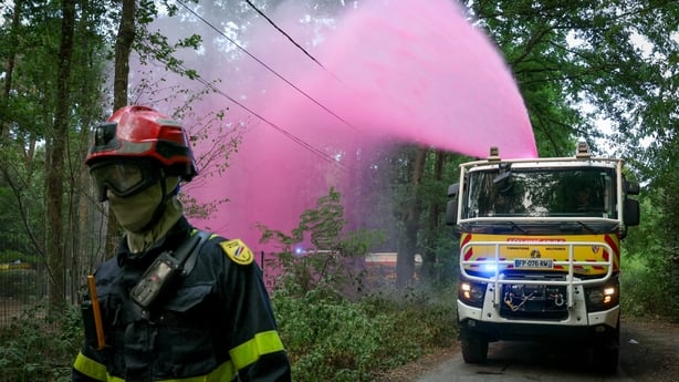 A fire truck sprays fire retardant as a firefighter walks ahead