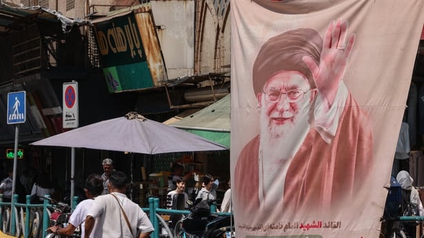 Iranians walk past a banner showing an image of Iran's slain supreme leader, Ayatollah Ali Khamenei, at Valiasr Square in Tehran