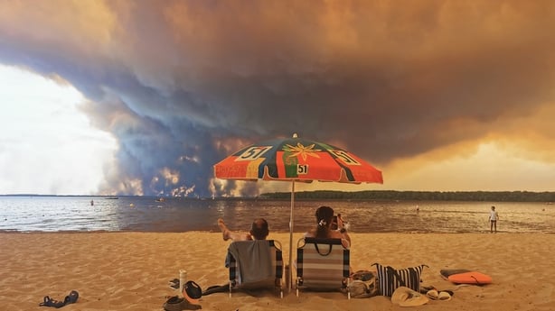 Beach goers rest on the beach of Moutchic on the shore of Lake Lacanau (Etang de Lacanau) in Lacanau , southwestern France on July 24, 2026, as clouds of smoke rise into the sky from the Gironde wildfire