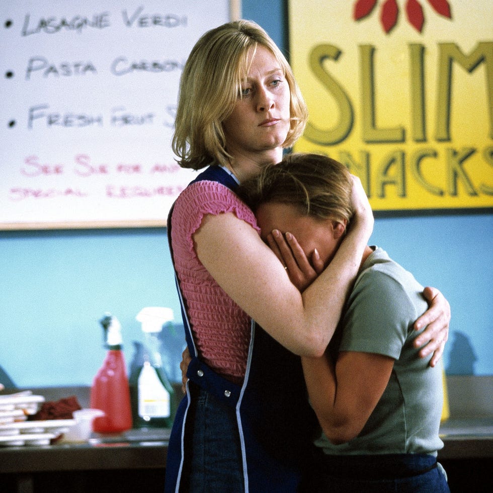 a woman hugs another person in front of a snack bar menu. a woman hugs another person in front of a snack bar menu.