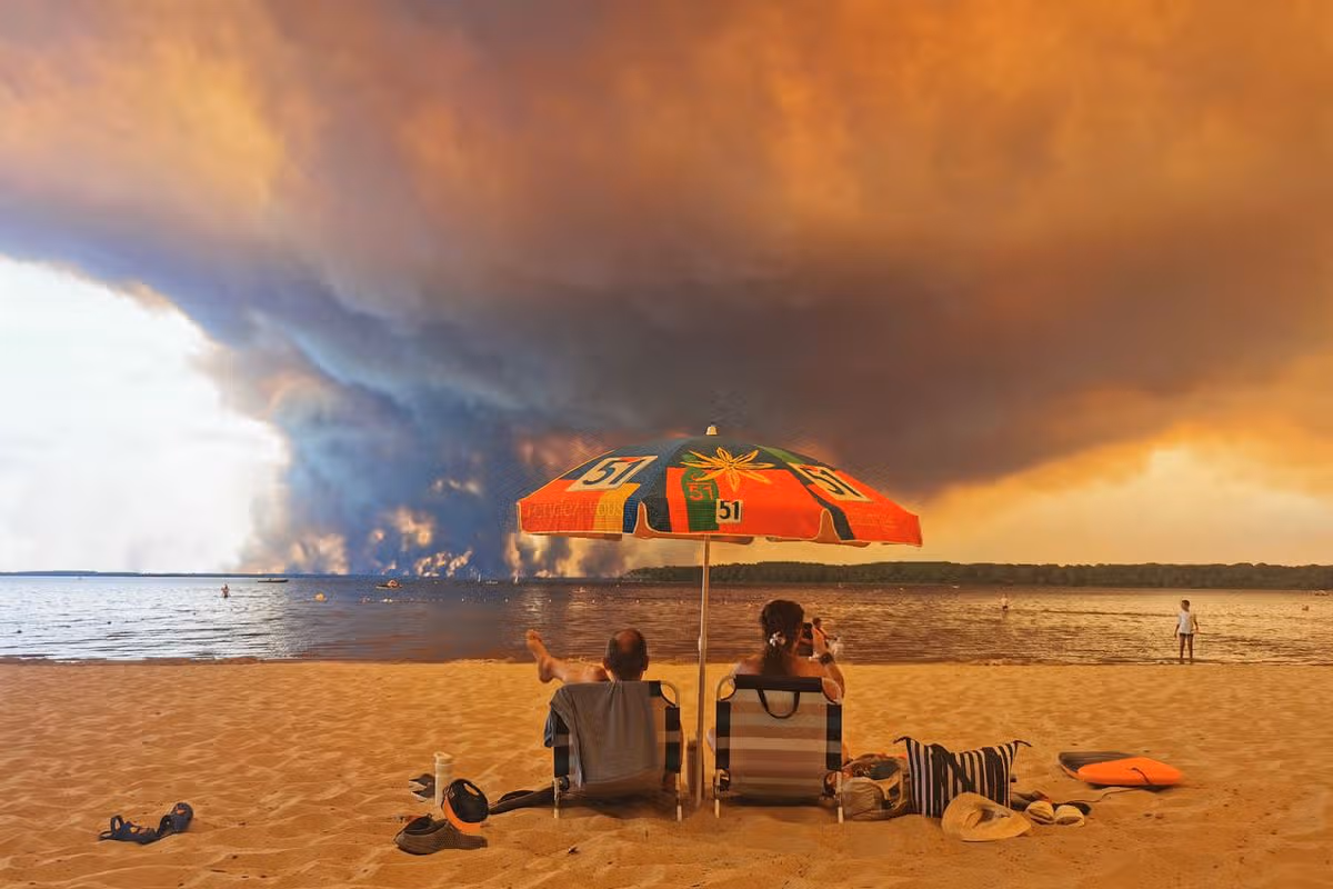 (FILES) Beach goers sit on the beach of Moutchic in Lacanau, southwestern France on July 24, 2026, as clouds of smoke rise into the sky from a wildfire. France has been battered by three heatwaves since May as part of increasingly common extreme weather episodes linked to climate change, causing thousands of excess deaths and fuelling wildfires. (Photo by Maximilien LAMY / AFP via Getty Images)
