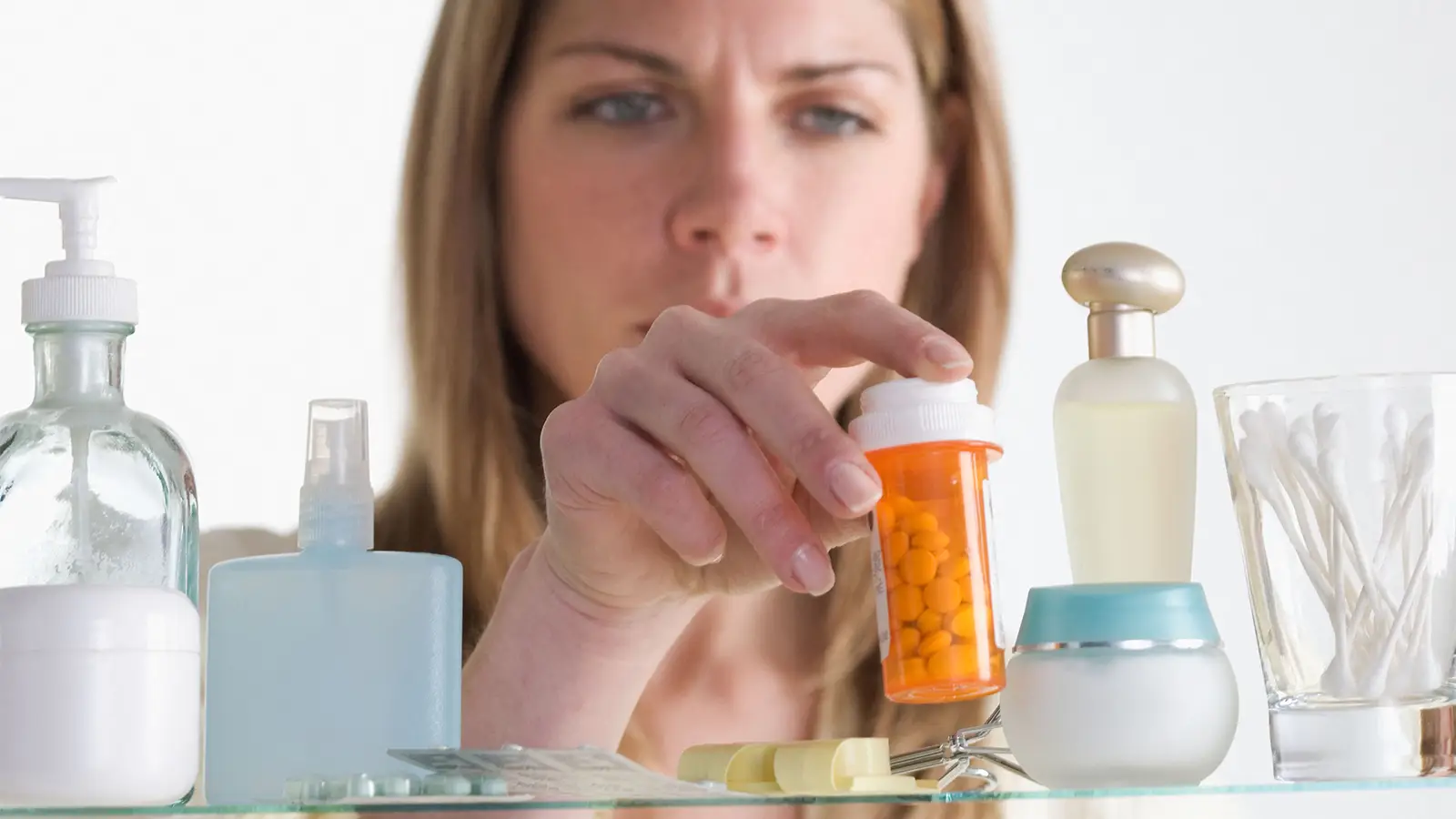 A photo of a woman reaching for a bottle of prescription medication from a medicine cabinet.