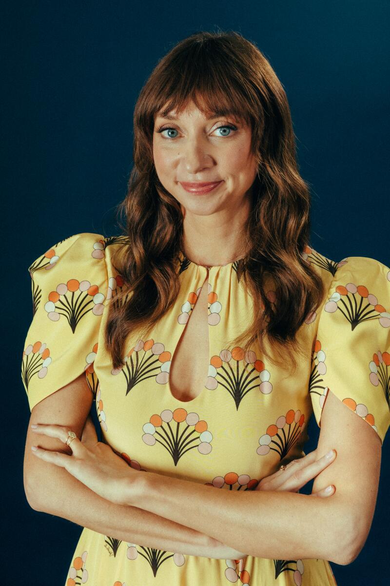 A woman with brown hair in a yellow dress with a colorful design.