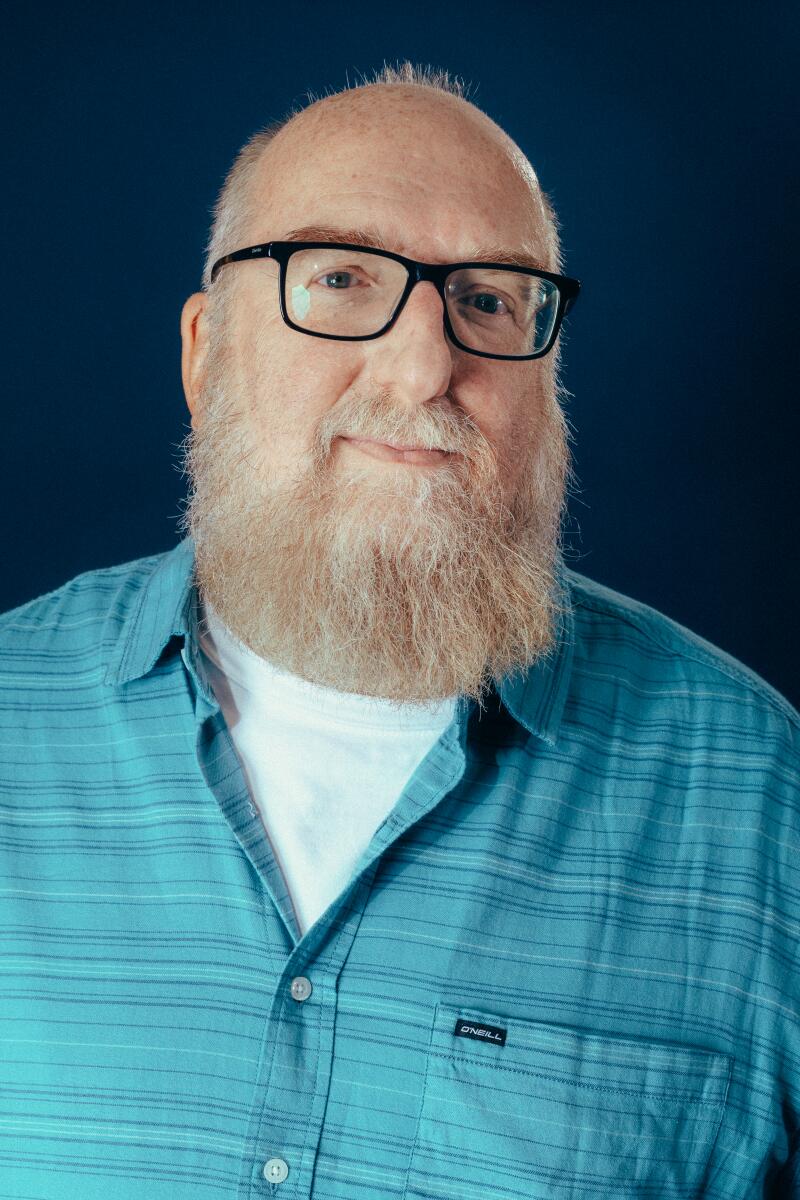 A bald man with black rimmed glasses in a blue shirt.