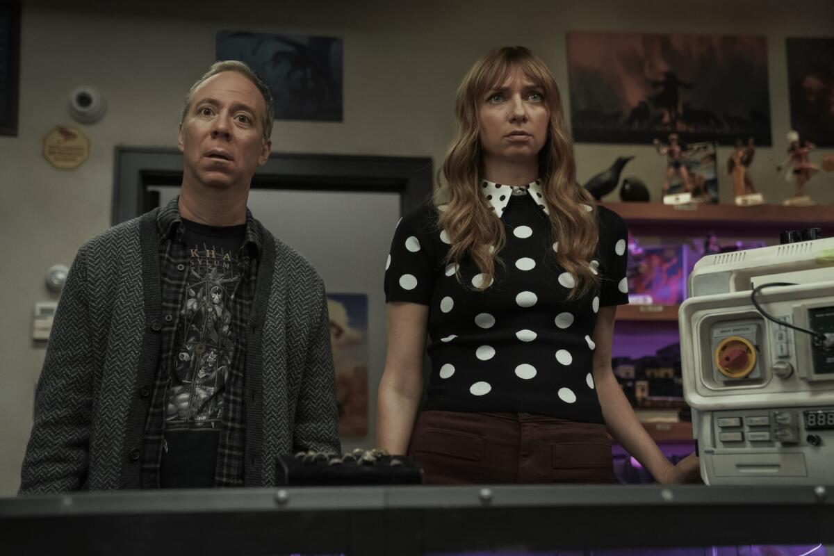 A man in a dark sweater and T-shirt stands next a frowning woman in a black and white polka dot shirt.
