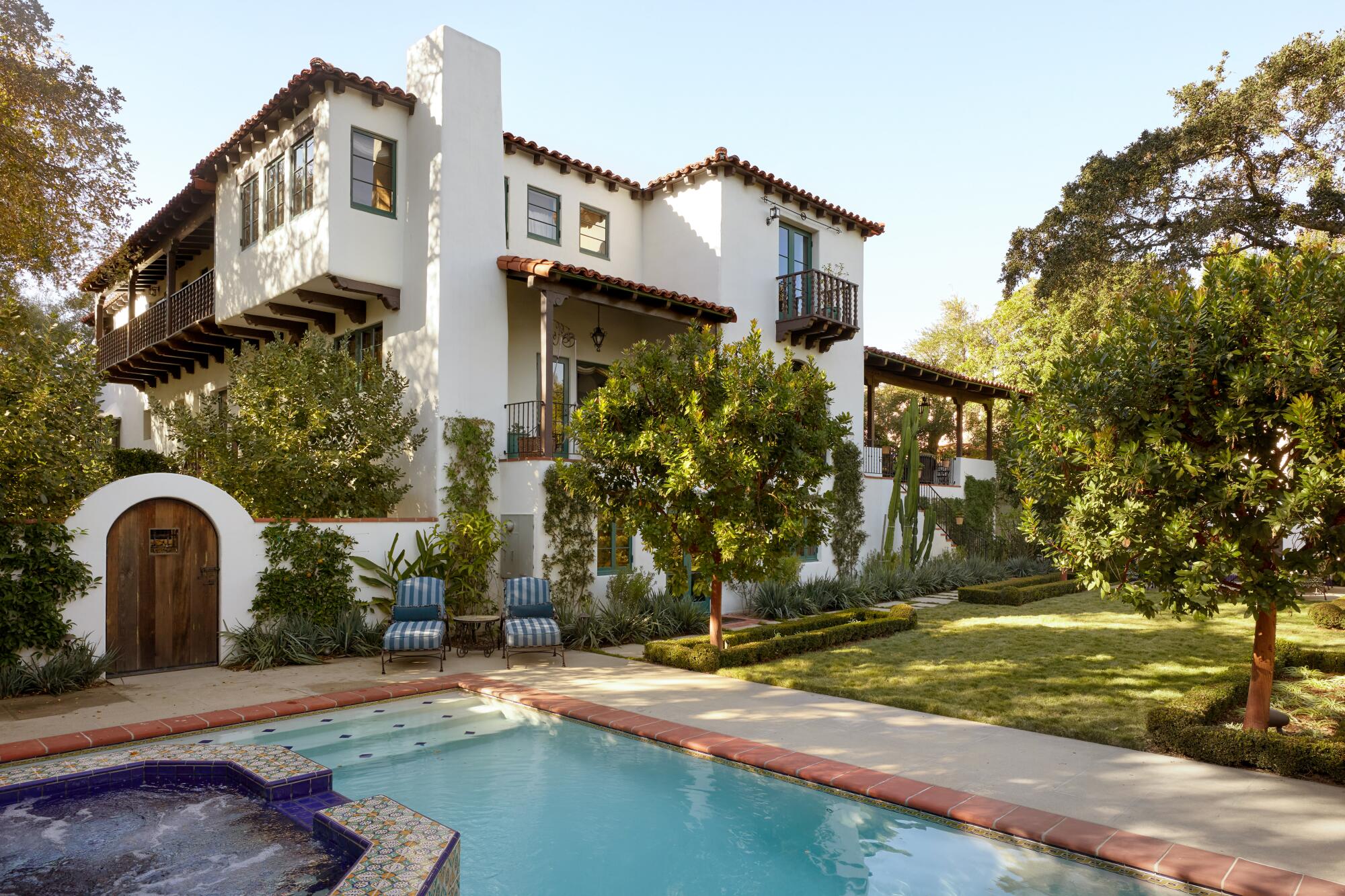 A large house behind a pool and green lawn,.