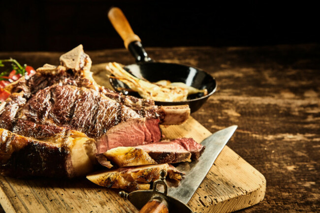 close-up-on-single-serving-of-rare-cooked-and-sliced-steak-next-to-knife-with-piece-of-roasted-garlic-over-wooden-cutting-board