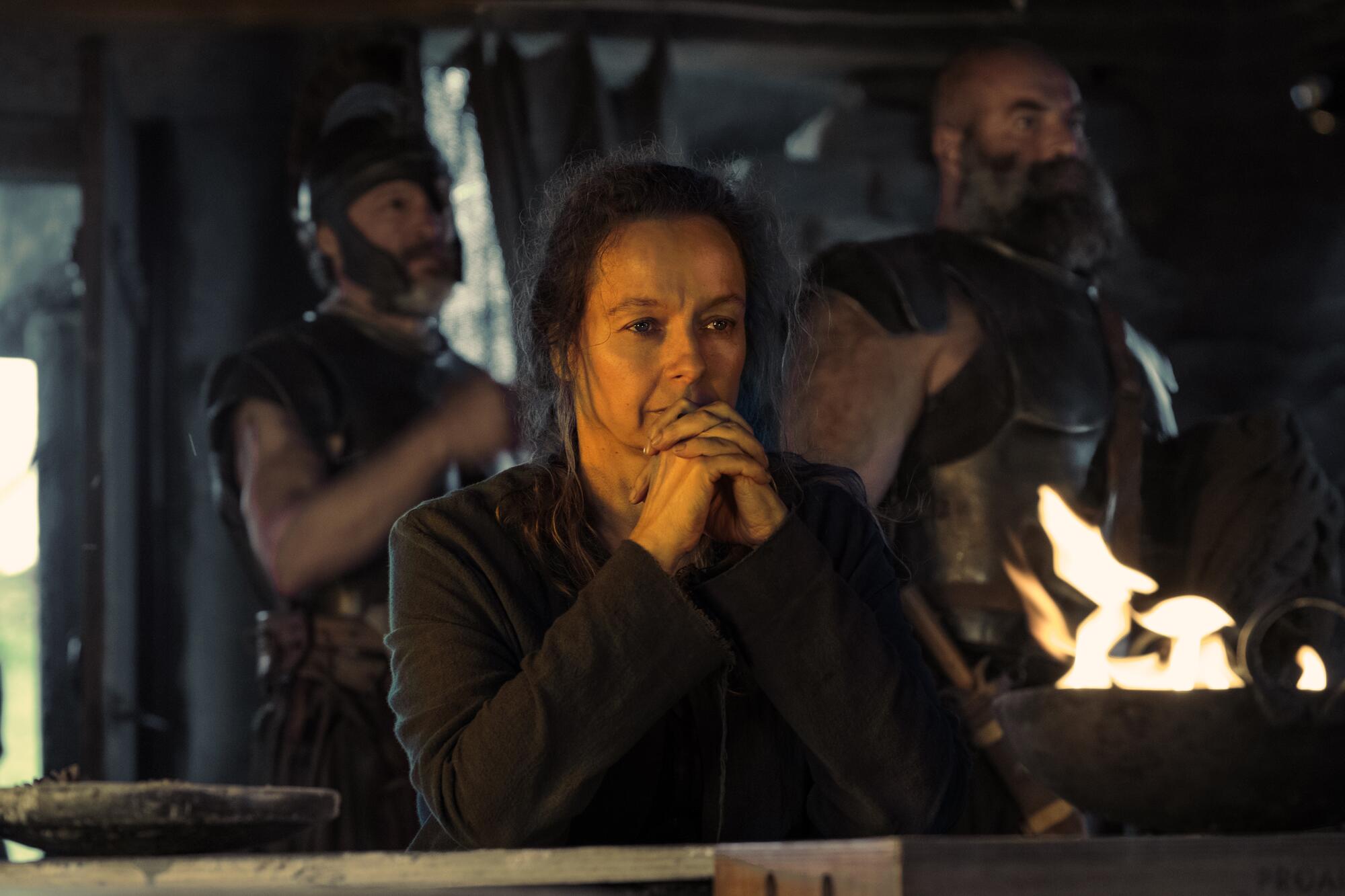 A woman sits in concentration by a fire.