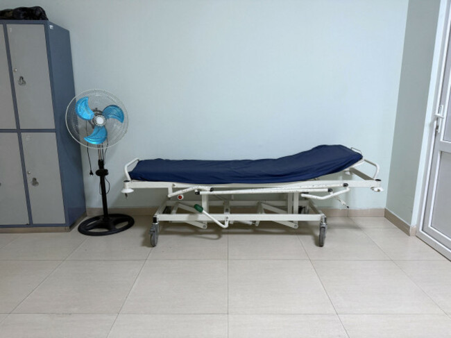 a-hospital-room-shows-a-stretcher-ready-for-use-next-to-a-fan-there-are-lockers-in-the-background-the-scene-appears-to-be-set-during-daytime