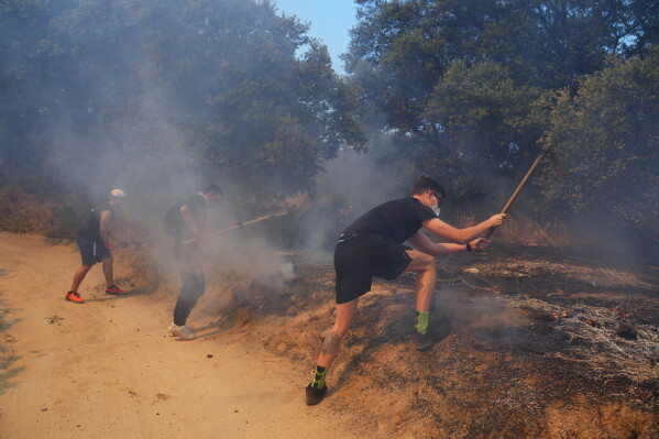 Volunteers try to help stop a wildfire from advancing in San Martin de Valdeiglesias, west of Madrid, Spain, Sunday, July 26, 2026. (AP Photo/Manu Fernandez)