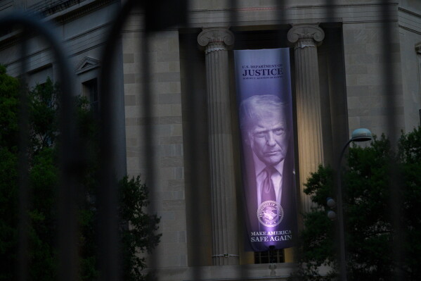 A portrait of President Donald Trump, is seen through a security fence on the Justice Department in Washington, Friday, July 24, 2026, as the White House Correspondents' Association dinner takes place nearby.. (AP Photo/Cliff Owen)